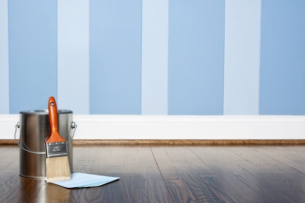 a blue striped wall behind a can of paint and a brush