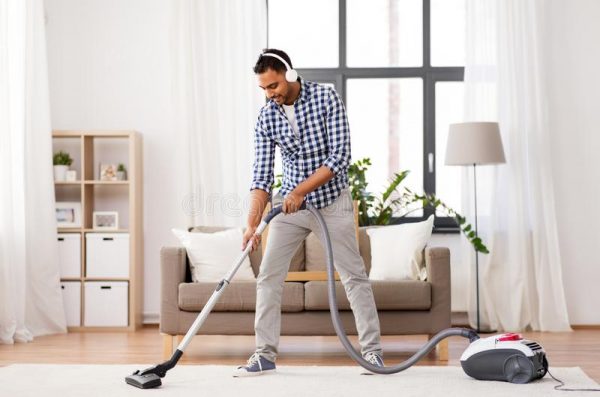 a man vacumming the carpet while listening to music with his headphones
